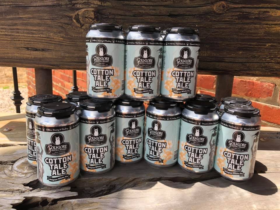 A bunch of cans of cotton tale ale are stacked on top of each other on a wooden table.