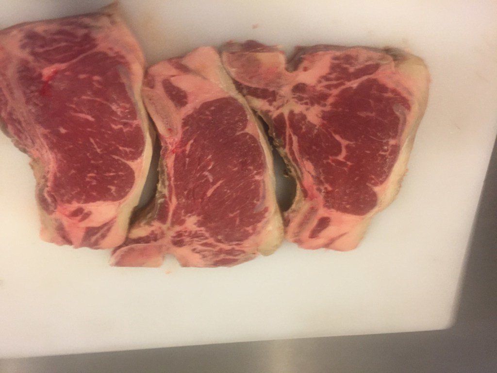Three raw steaks are sitting on a white cutting board.