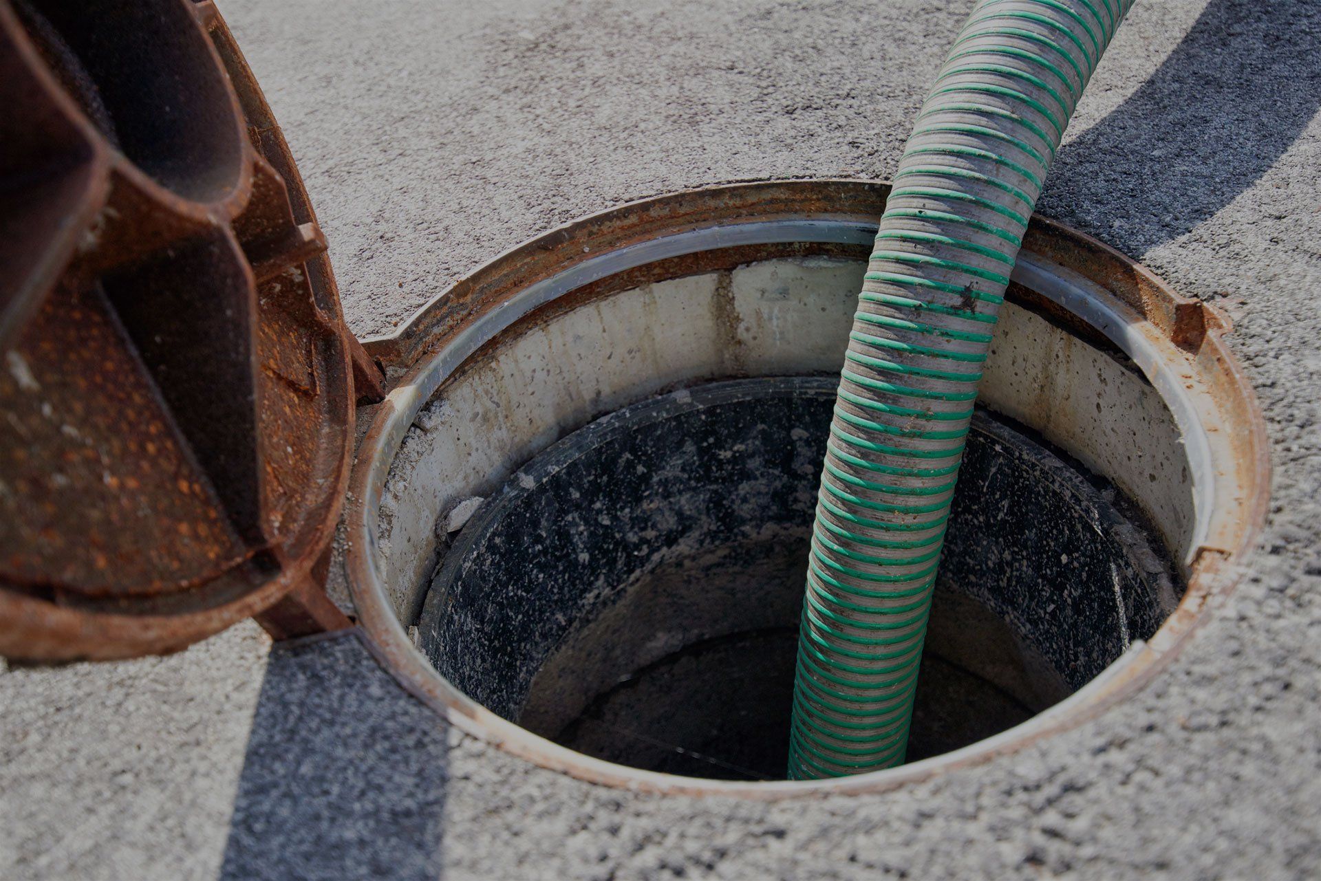 Open sewer manhole with a green hose inside.