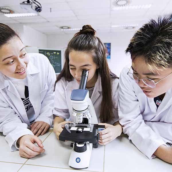Three people are looking through a microscope in a lab.