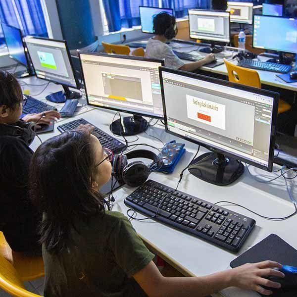 A group of people are sitting in front of computer monitors.