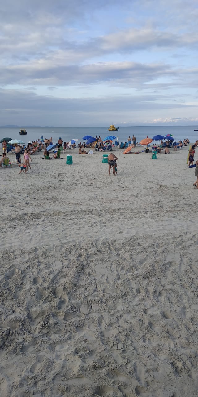 Uma praia cheia de gente e guarda-sóis em um dia ensolarado.