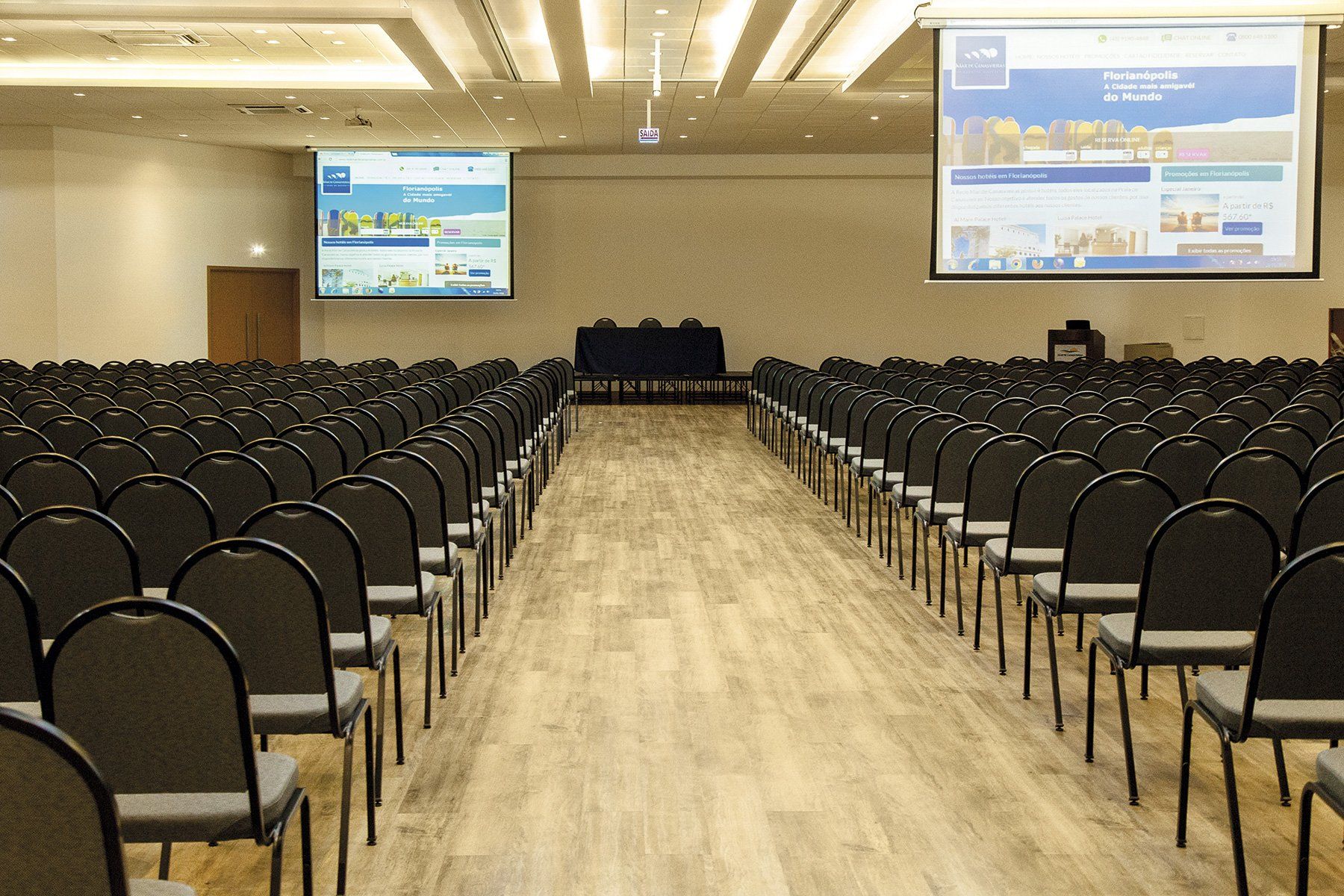 Uma grande sala de conferências com fileiras de cadeiras e uma tela de projeção.