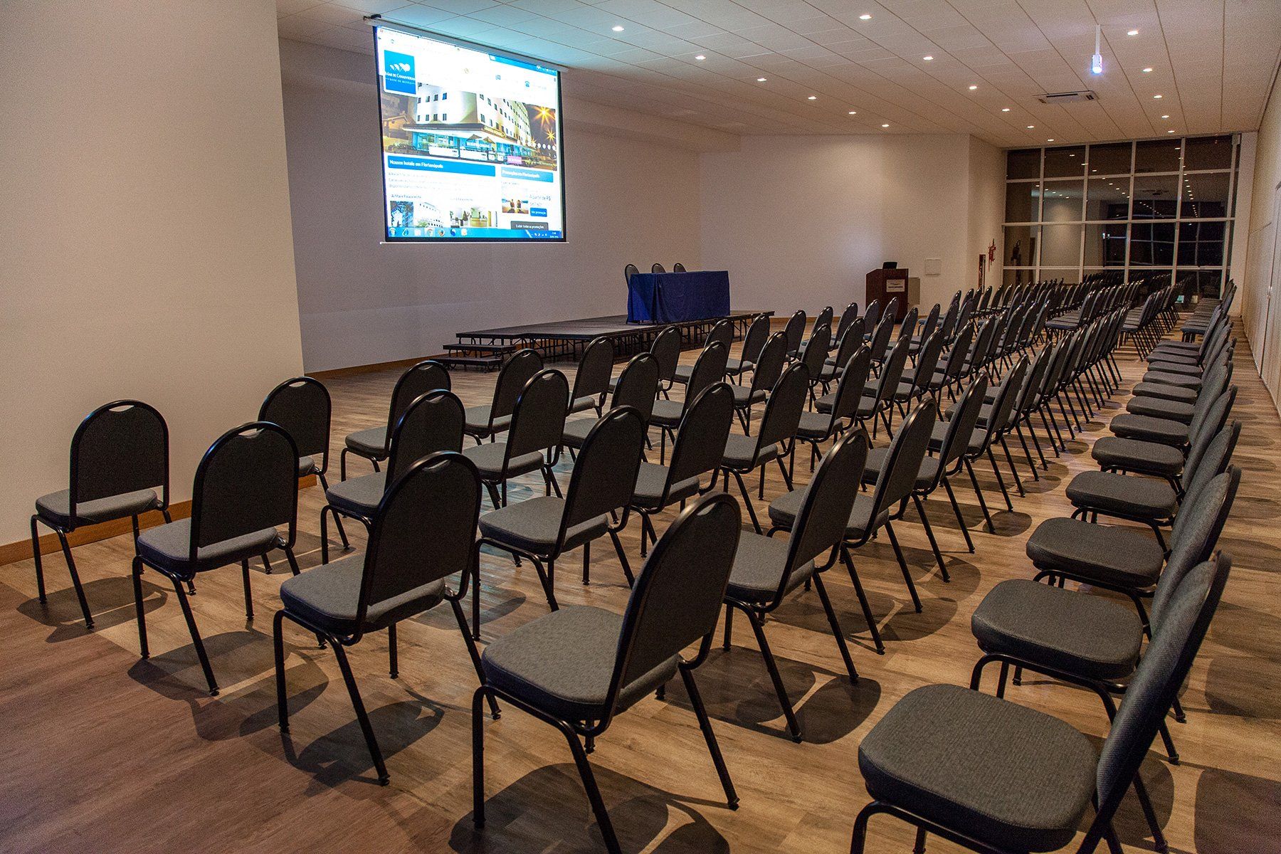 Uma grande sala de conferências com fileiras de cadeiras e uma tela de projeção.