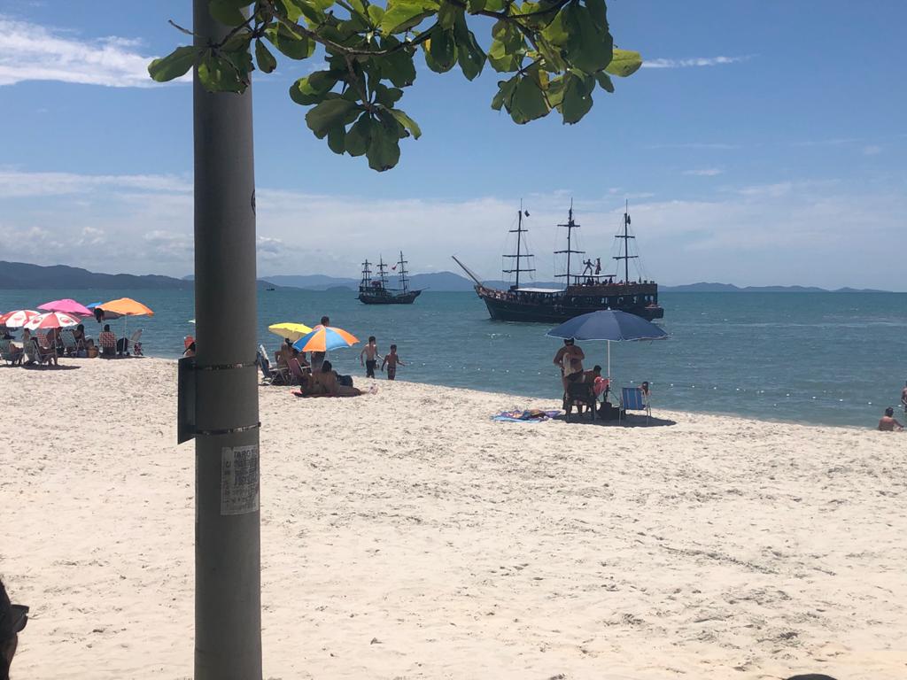 Um grupo de pessoas está na praia com um barco ao fundo.