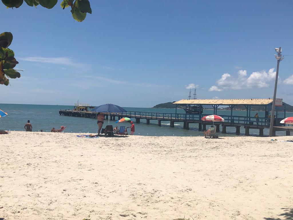 Uma praia com cadeiras e guarda-sóis e um cais ao fundo