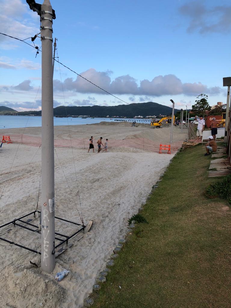 Um grupo de pessoas caminha em uma praia próximo a um poste.