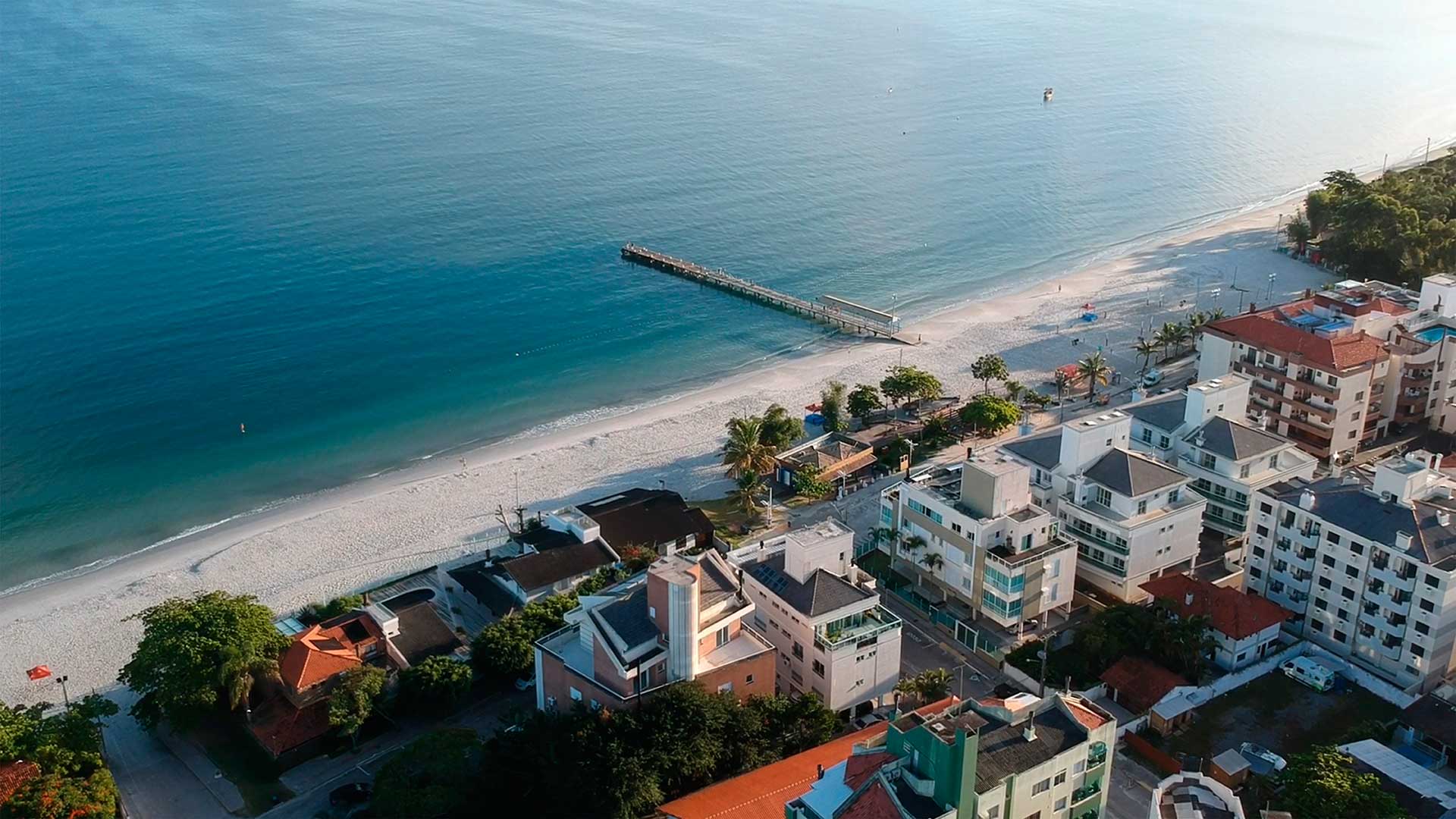 Uma vista aérea de uma praia com edifícios e árvores junto ao oceano.