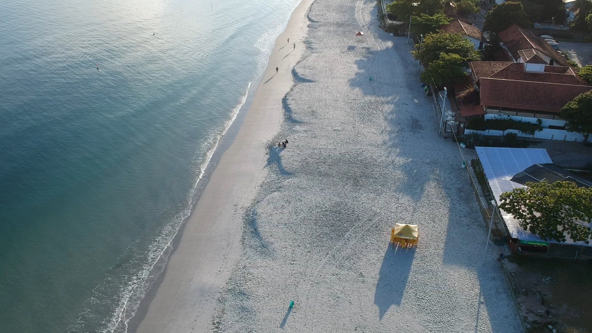 Uma vista aérea de uma praia com um guarda-chuva amarelo.