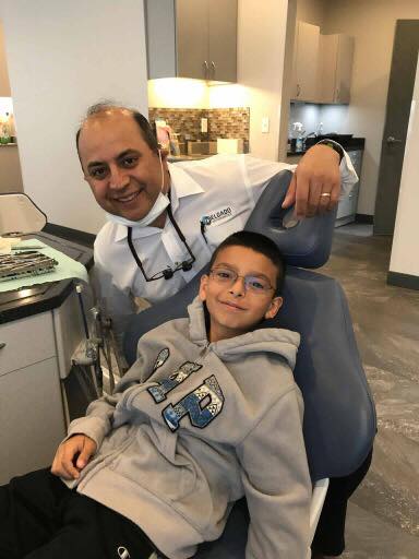 Dentist and child in dental chair; dentist smiles, puts arm on the chair.