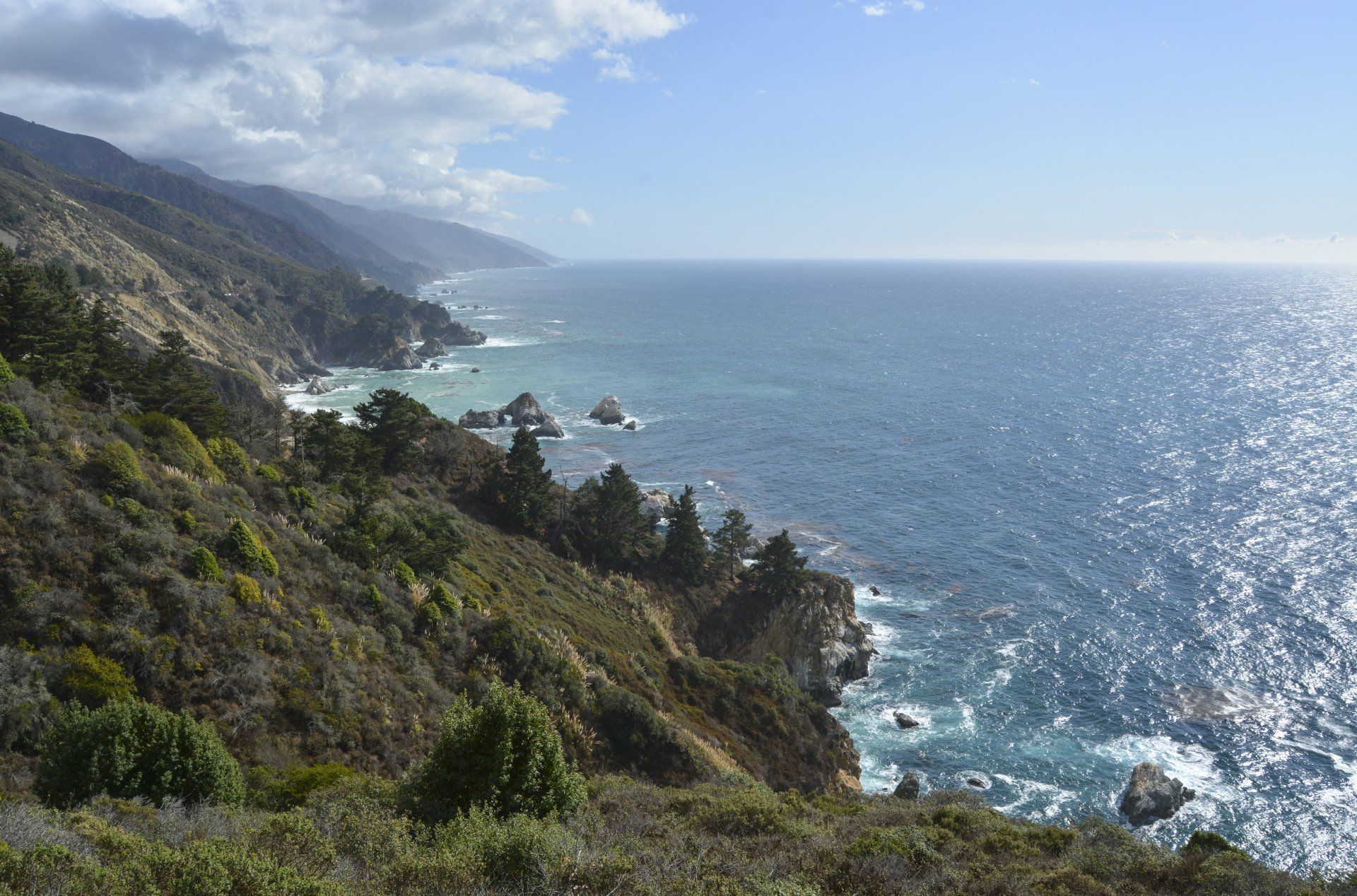 Coastal view with mountains and ocean under a bright, sunny sky.