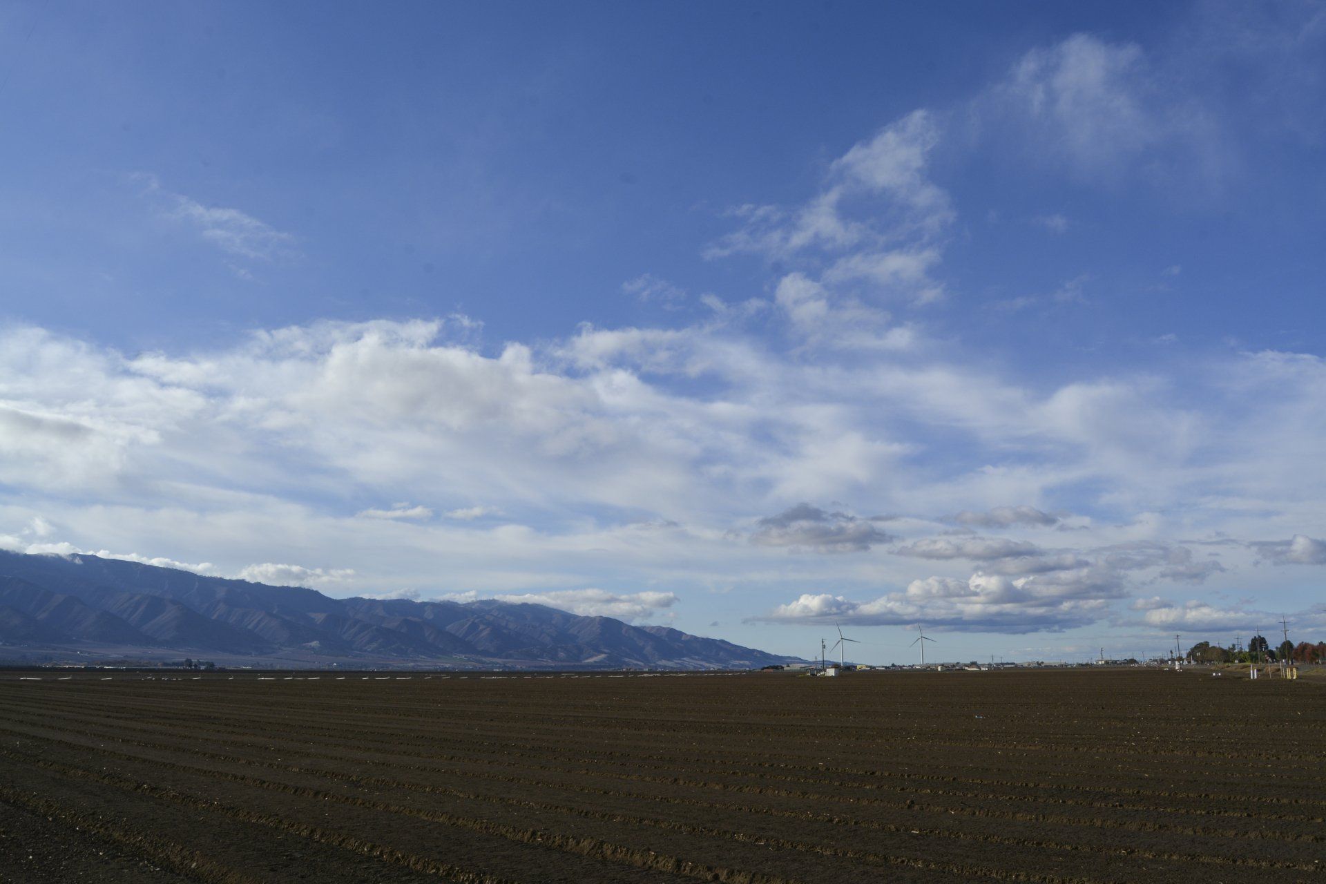 Arable brown field under a partly cloudy blue sky, with mountains in the background.