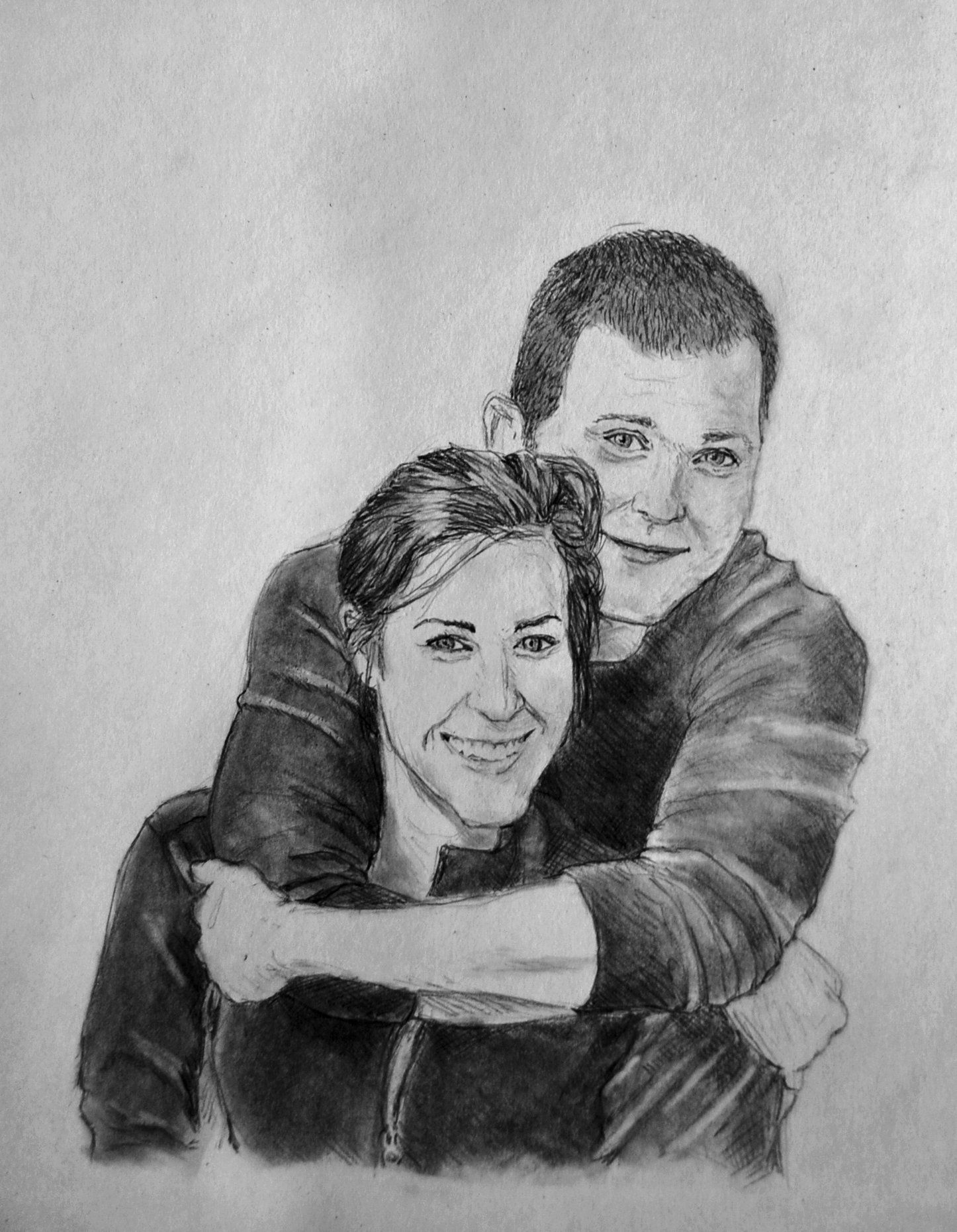 A smiling woman is hugged from behind by a smiling person; both looking towards the viewer.