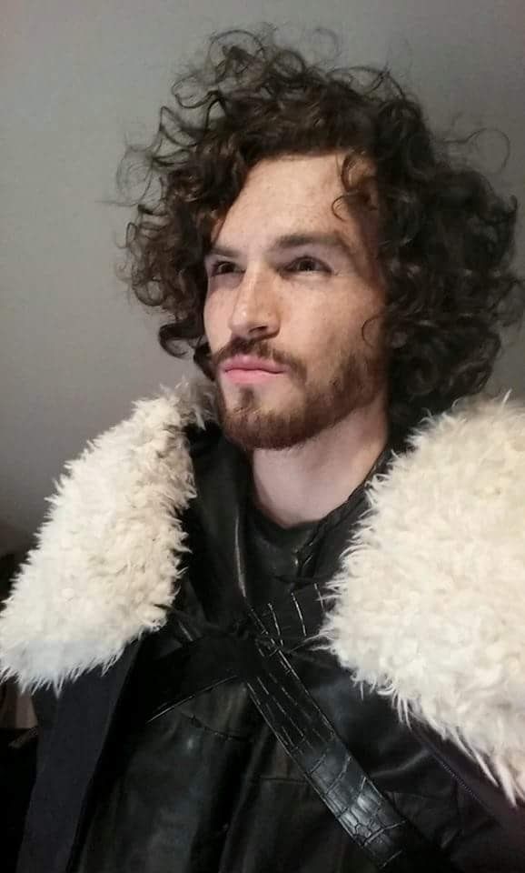 Man with curly hair and beard wearing a black leather jacket with a white fur collar.