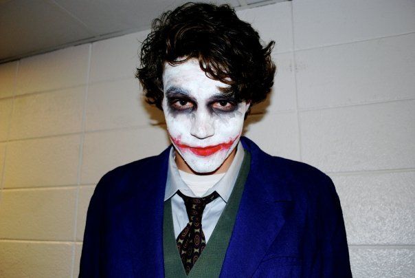 Person in Joker costume with white face paint, red lips, and dark eye makeup. Wearing a blue jacket.