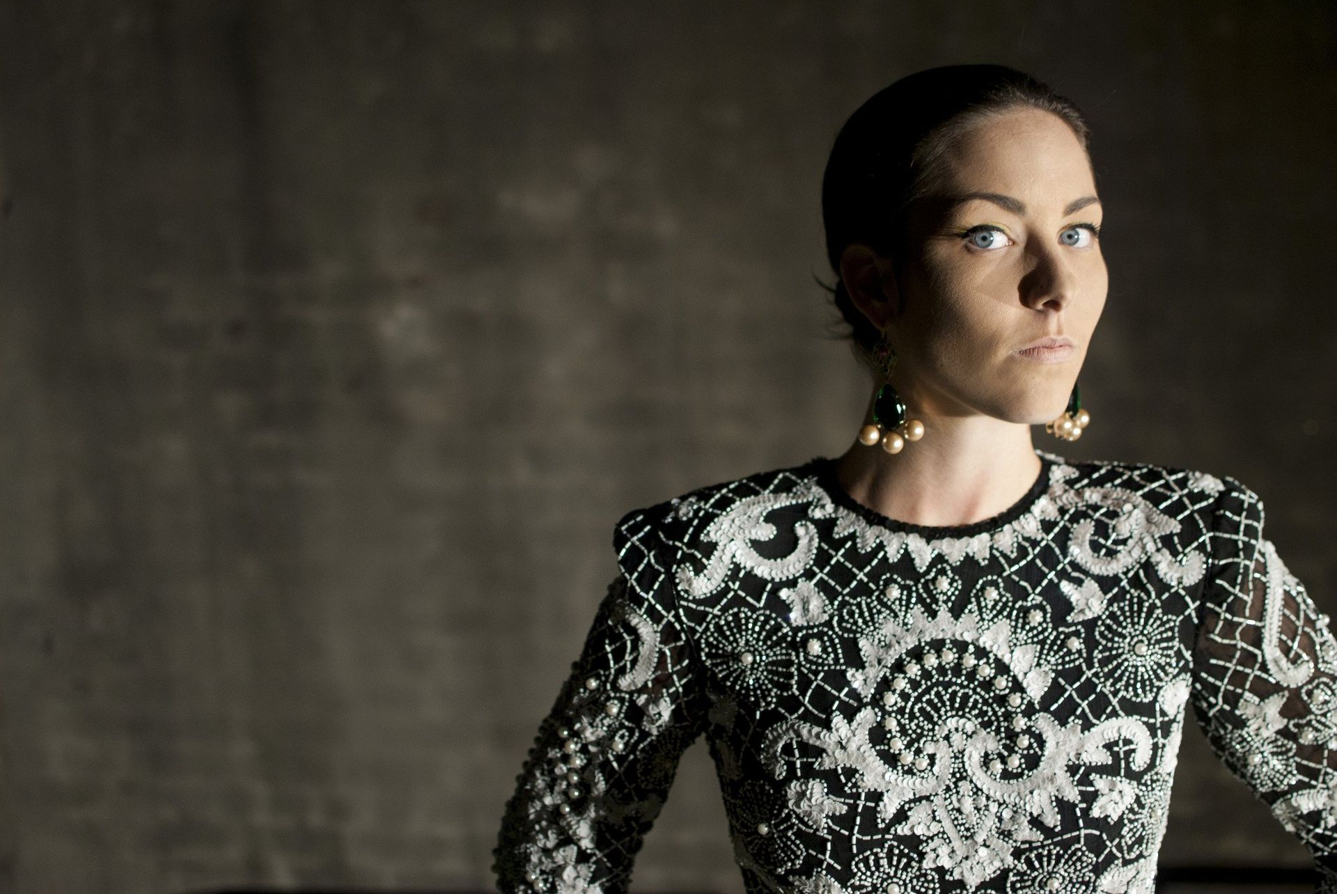 Woman wearing a beaded, decorative top and large earrings poses in front of a dark background.