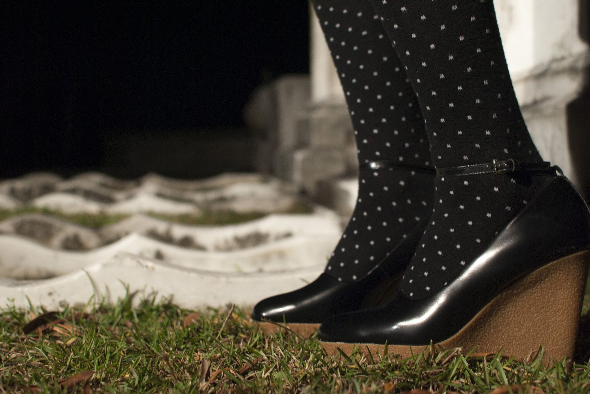 Black wedge heels, dotted stockings, grass, and a tomb.