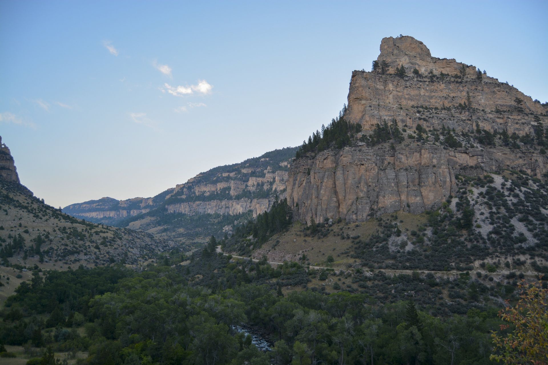 Mountain landscape, rocky cliffs, trees, valley, and a blue sky.