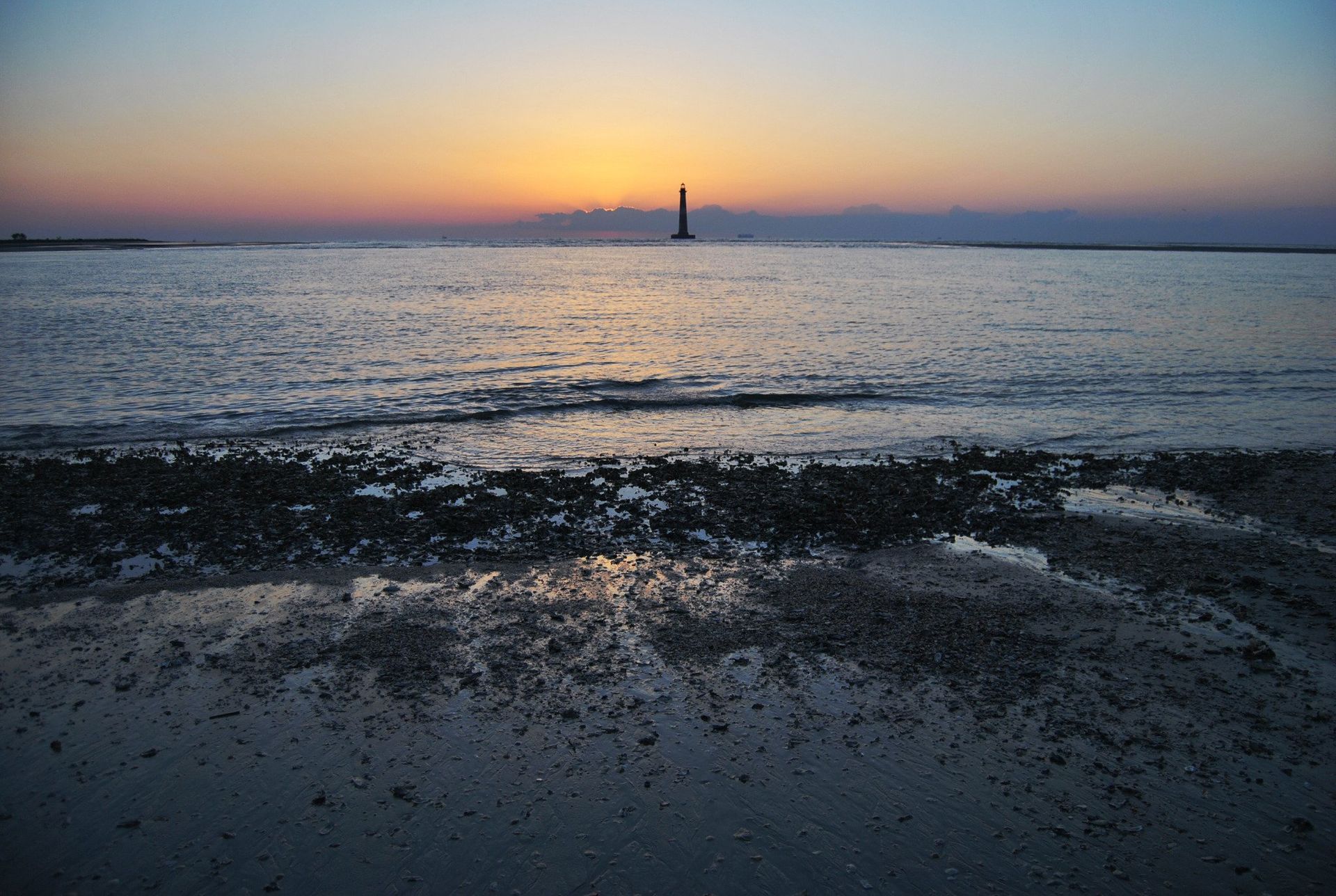 Sunset over the ocean, silhouette of a sailboat on the horizon.