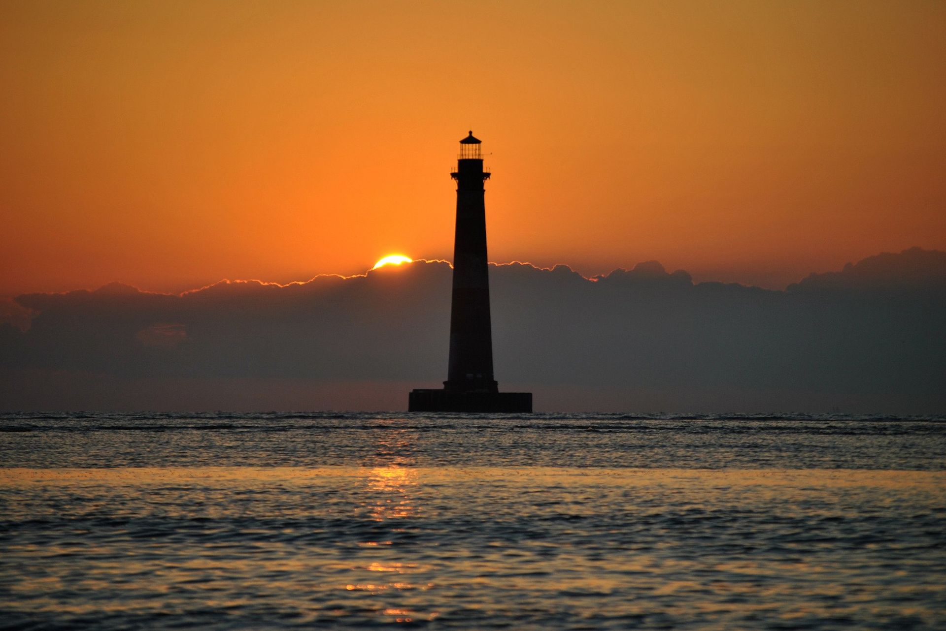 Lighthouse silhouette against an orange sunset over the water.