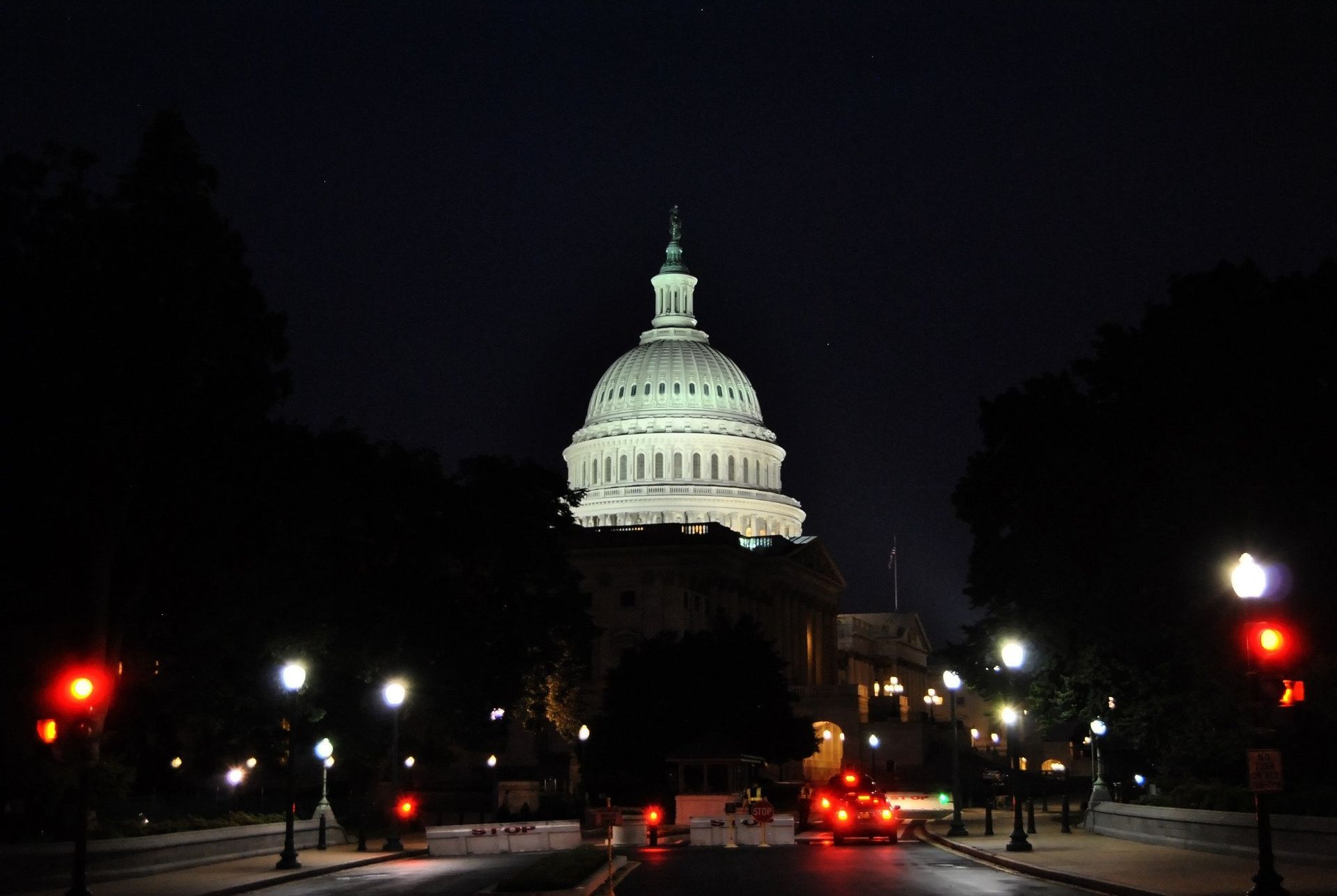 United States Capitol building illuminated at night, viewed from a road lined with trees and streetlights.