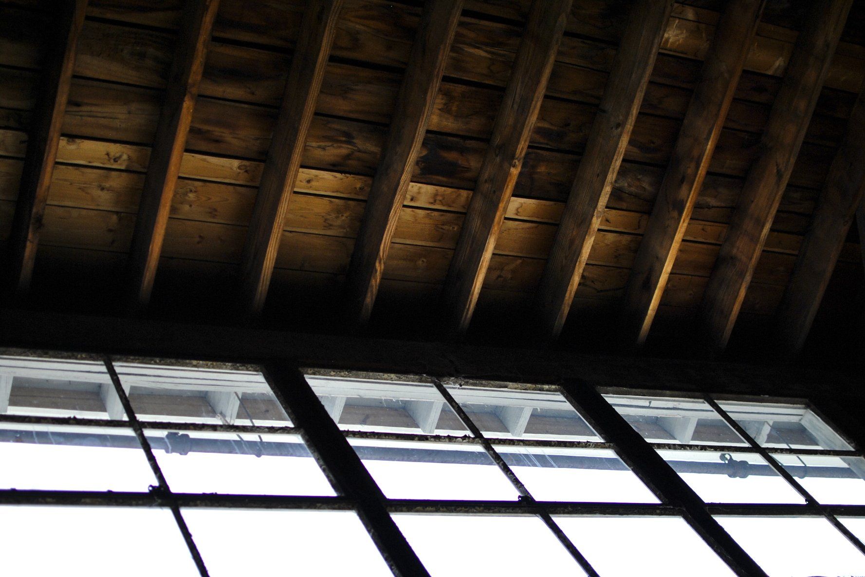 Wooden ceiling with exposed beams above a large window with black frames.