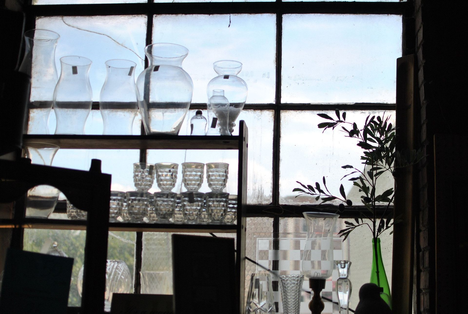 Glassware on a shelf in front of a window; some panes are cracked.