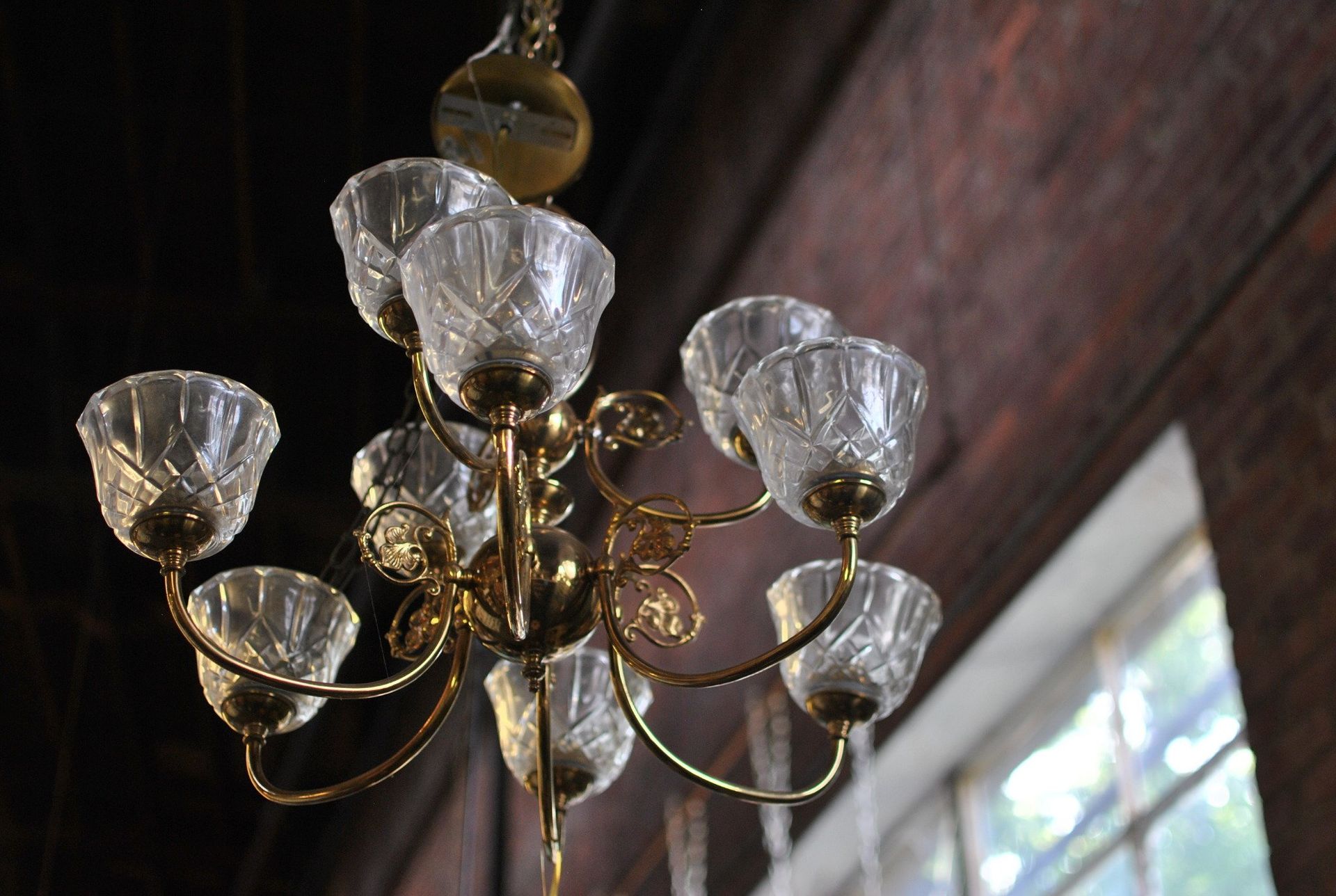Ornate gold chandelier with glass shades hanging from a wood ceiling, near a window.