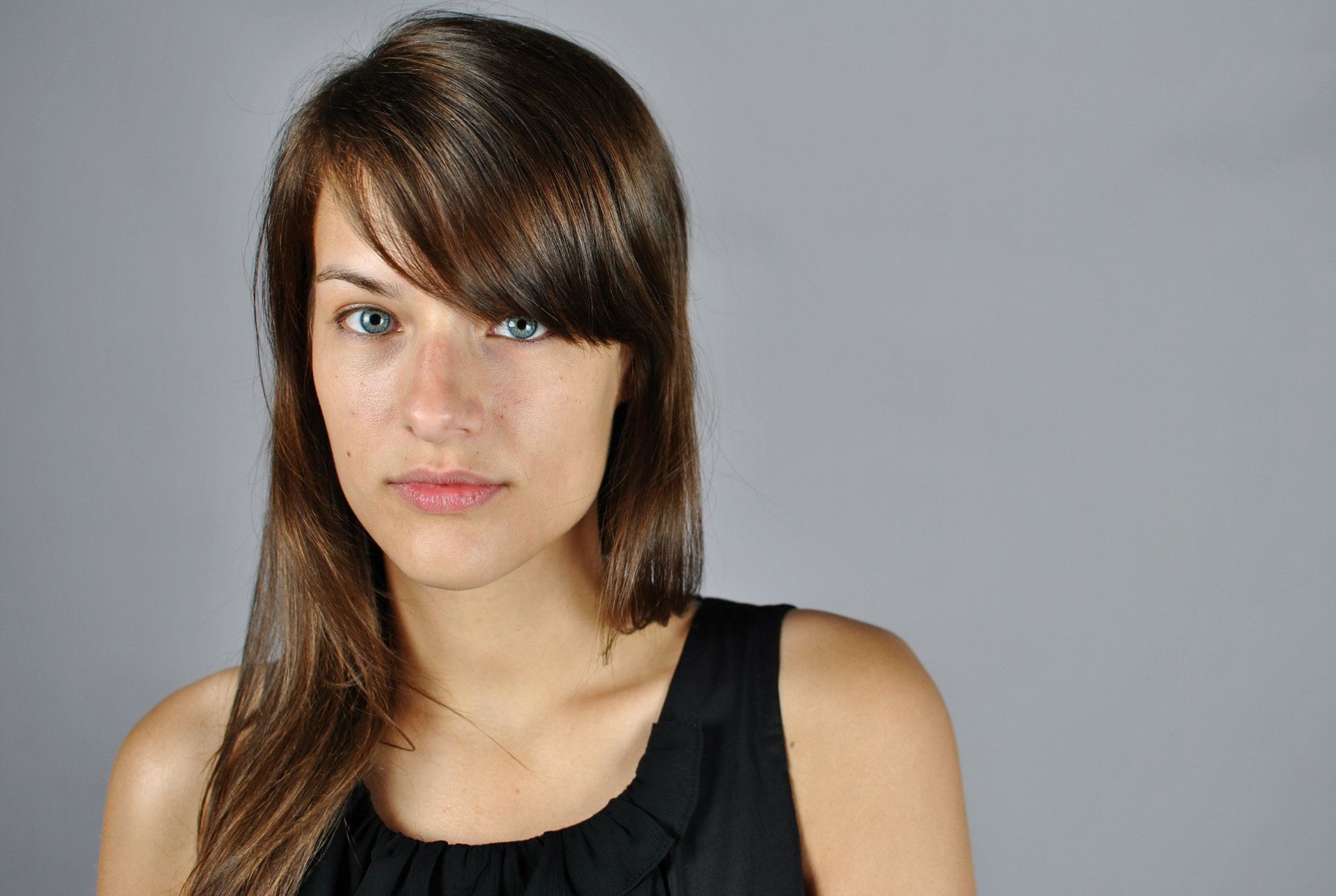 Woman with brown hair and bangs, wearing a black top, looks directly at the camera.