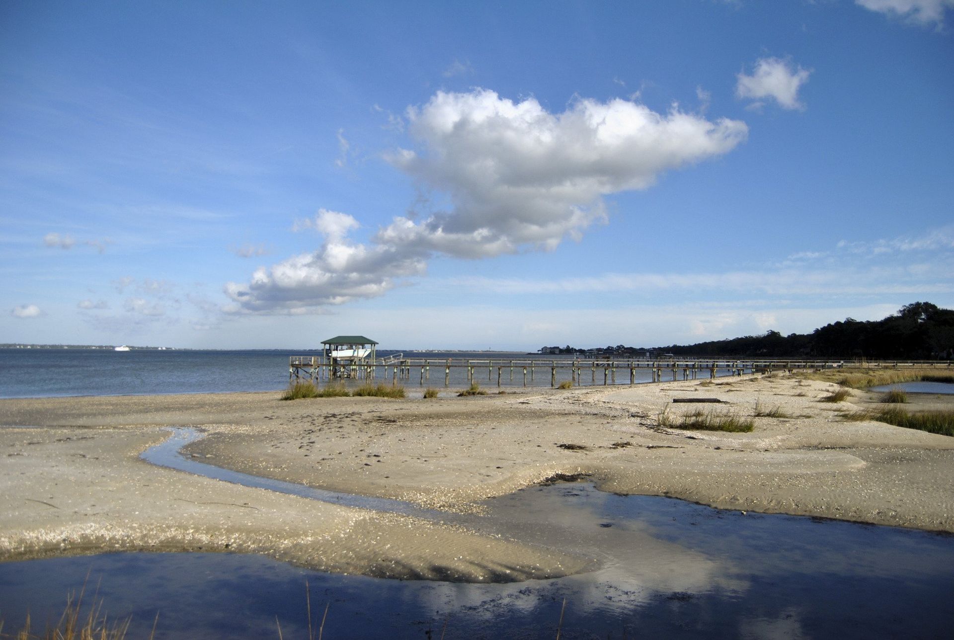 Beach scene with a small building on stilts, cloudy sky, and a stream flowing into the water.