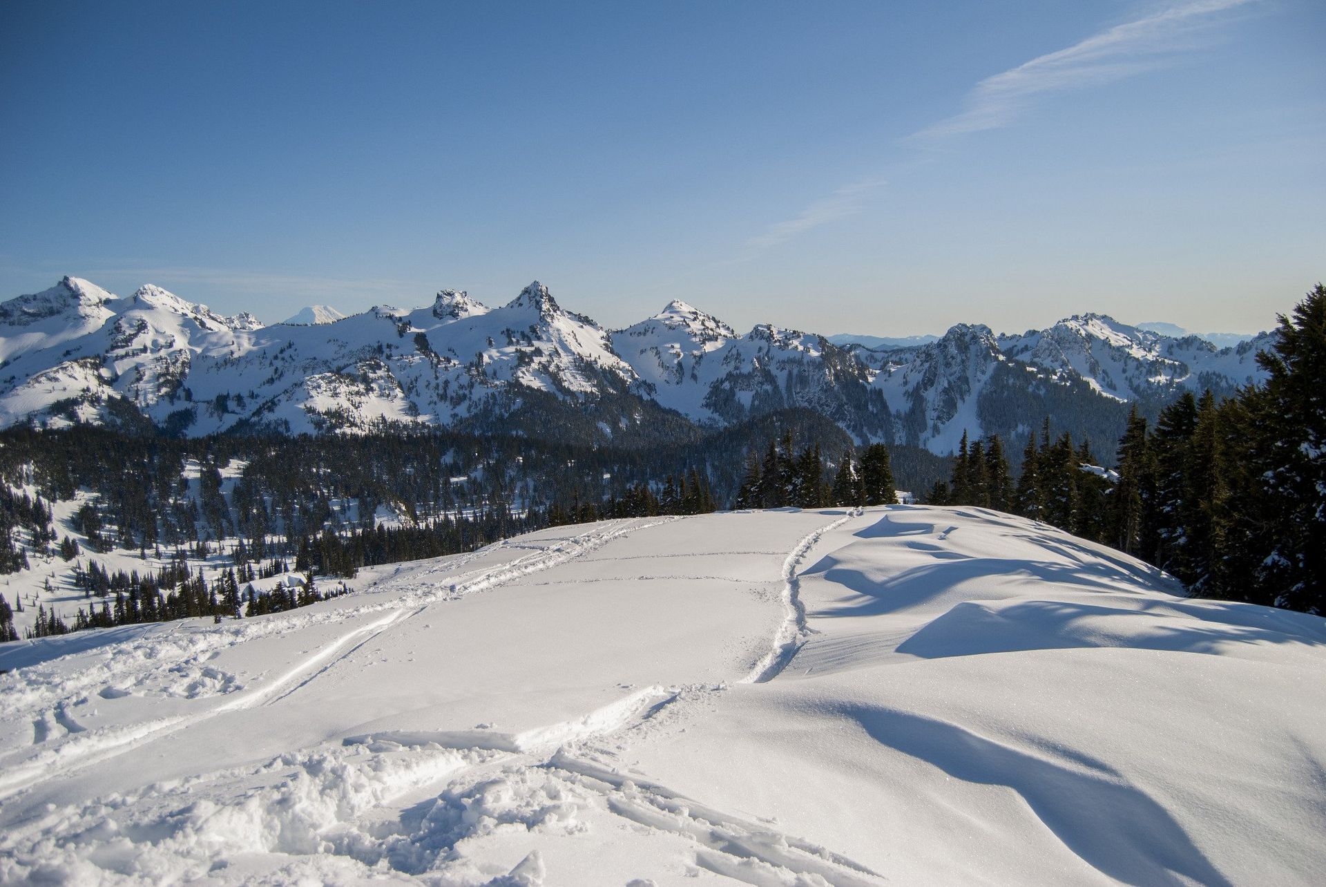 Snowy mountain range under a clear blue sky. Snow covers the foreground and peaks.