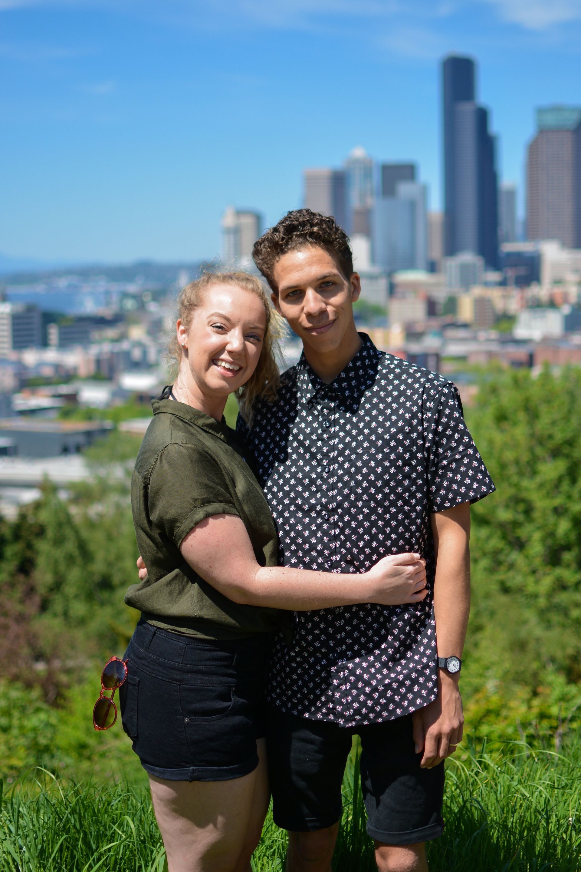 Couple hugging, smiling, with city skyline in the background on a sunny day.