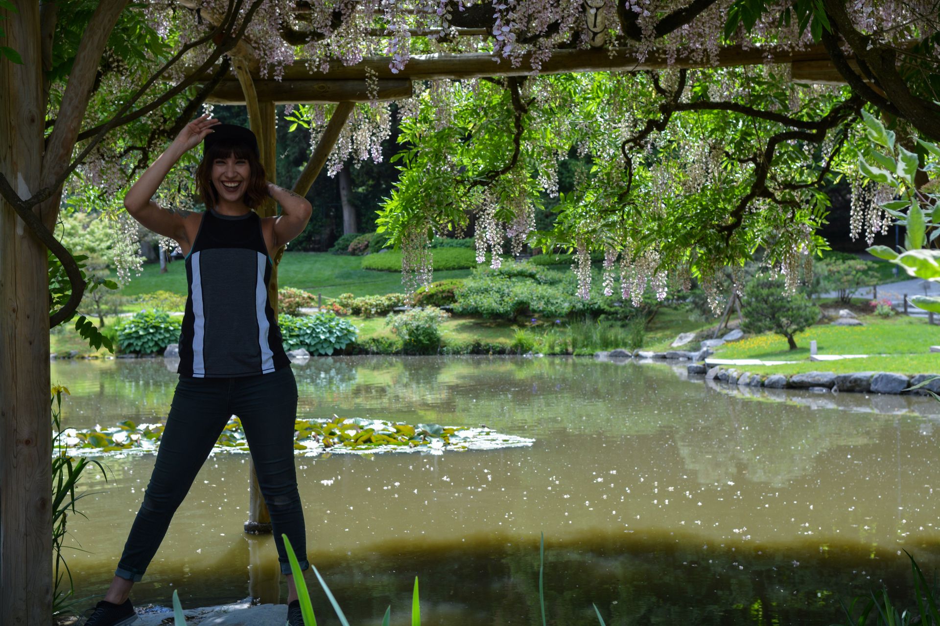 Woman poses under flowering arbor by a pond.