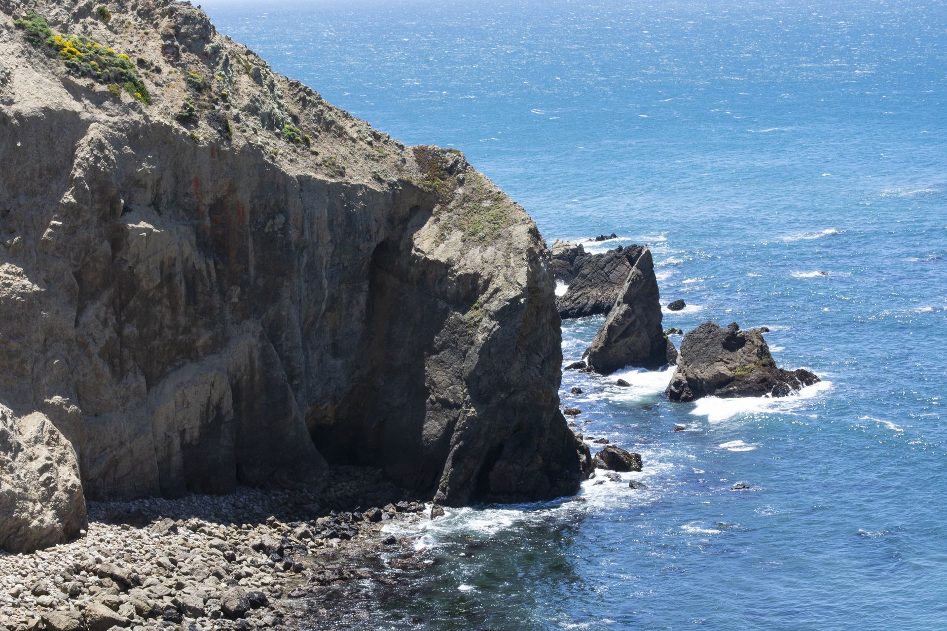 Rocky cliffside overlooking a blue ocean, with rock formations and a bright sky.