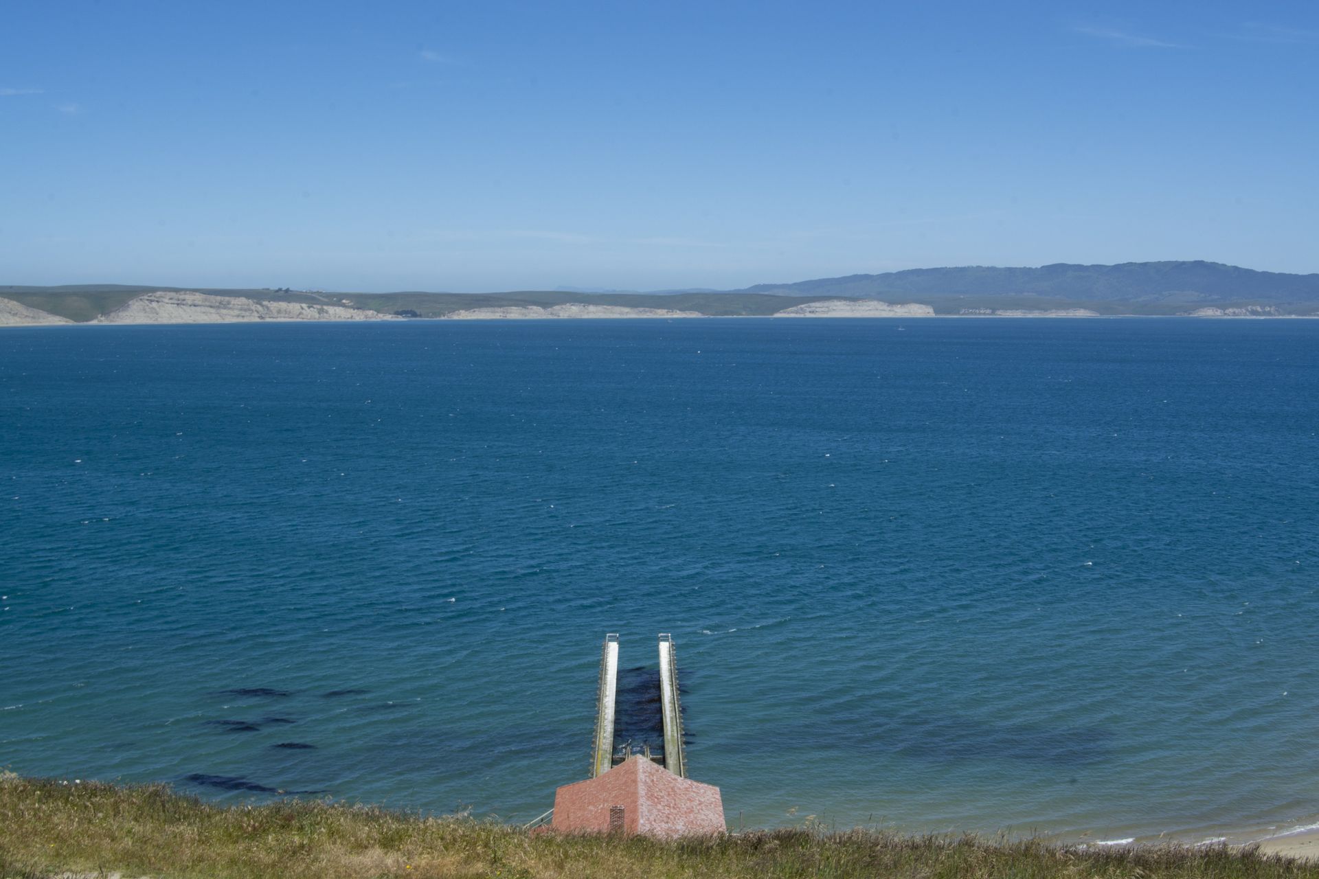 Blue ocean view with a ramp leading into the water, and a distant coastline under a clear blue sky.