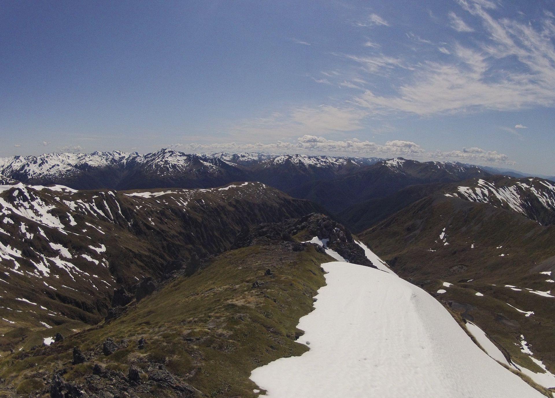 Snow-covered mountain ridges under a blue sky, with some green vegetation.