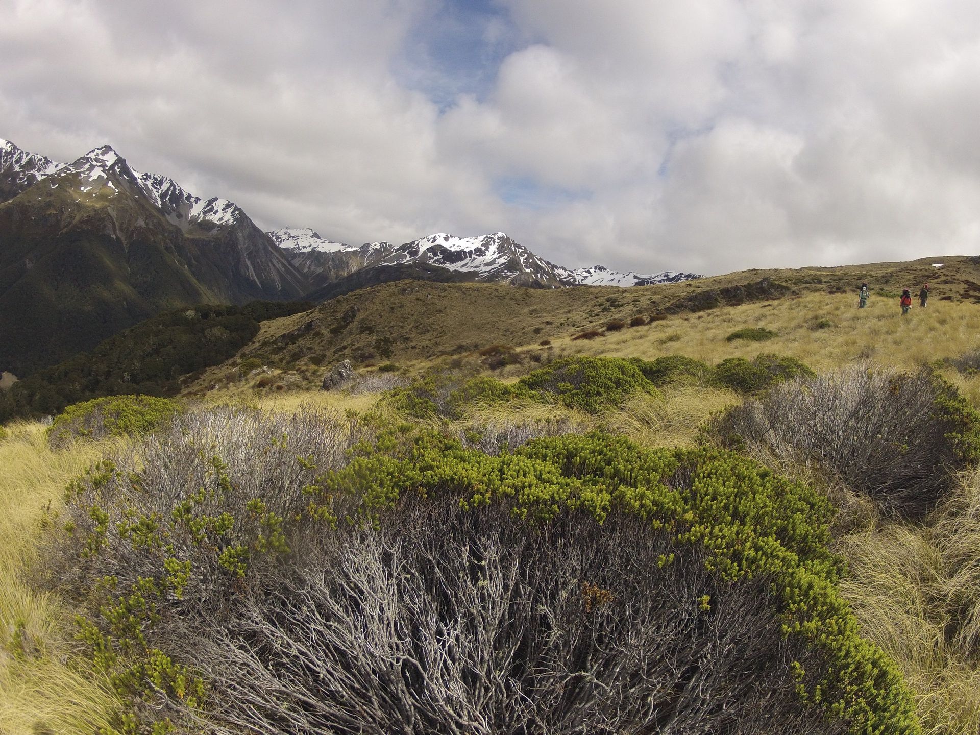 Hiking trail with mountains in the background, some snow-capped. Sunny with scattered clouds.