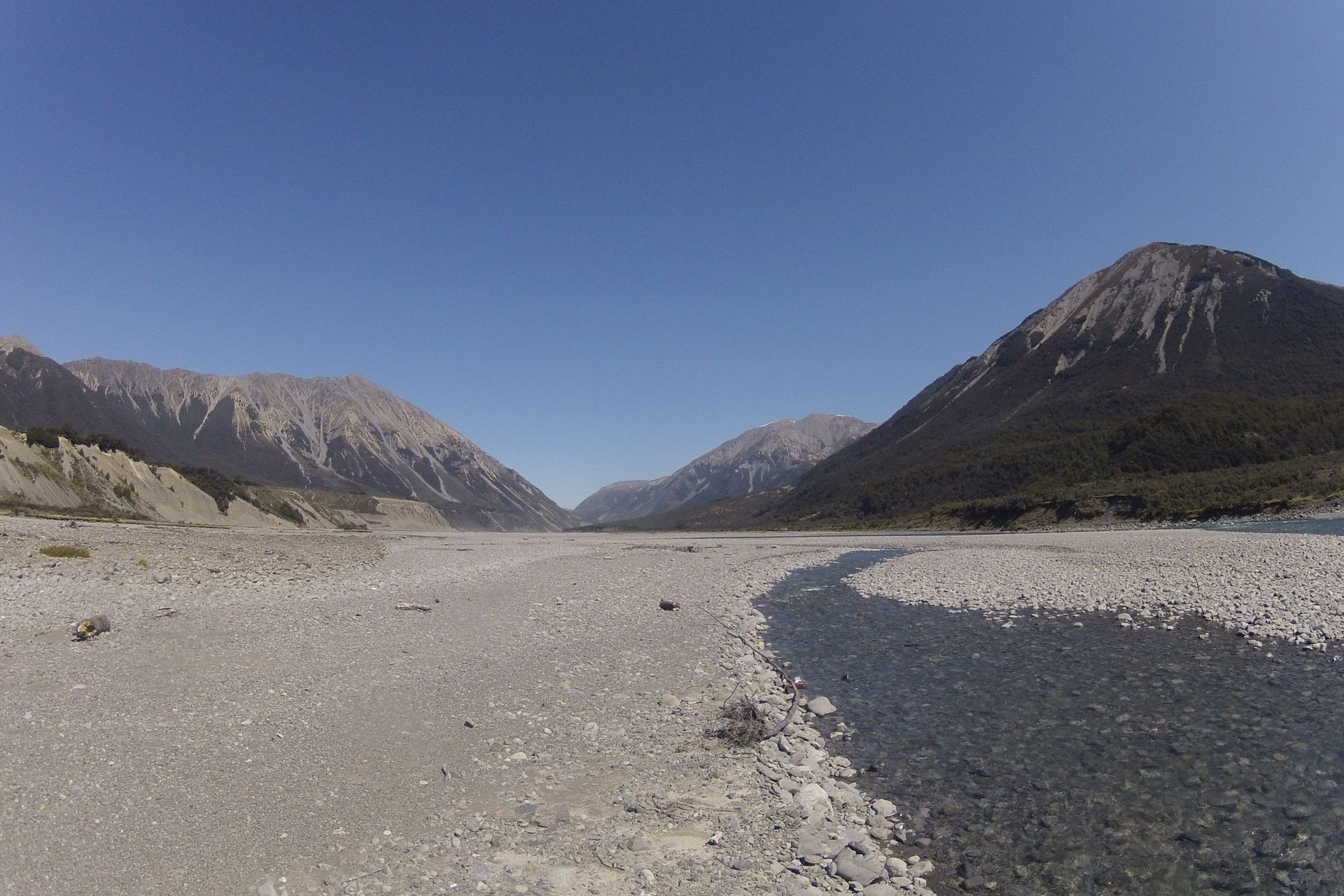 Rocky riverbed winding through a mountain valley under a clear blue sky.