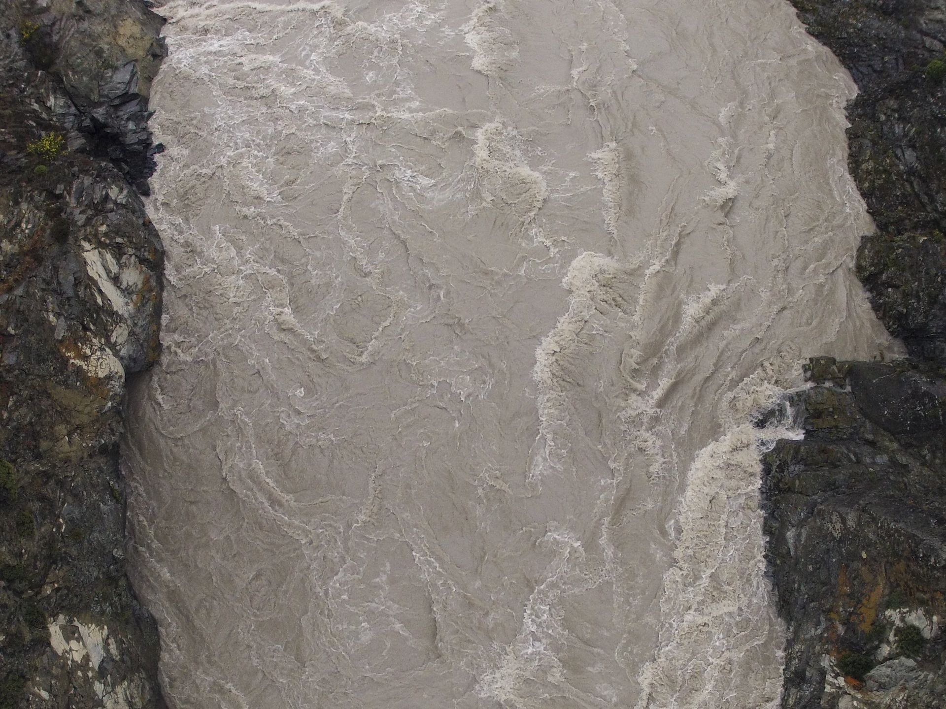 Turbid river flowing between dark rocky banks.