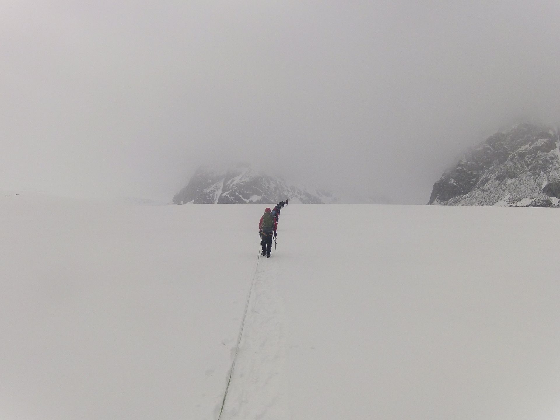 Person trekking across snow-covered plain, pointing towards distant mountains shrouded in fog.