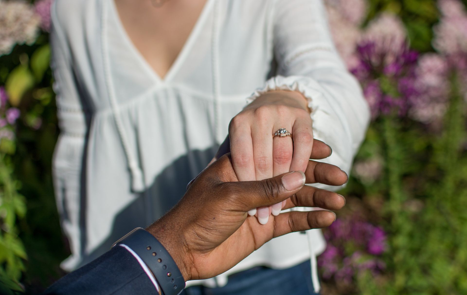 Hands clasped, engagement ring on one hand, floral background.