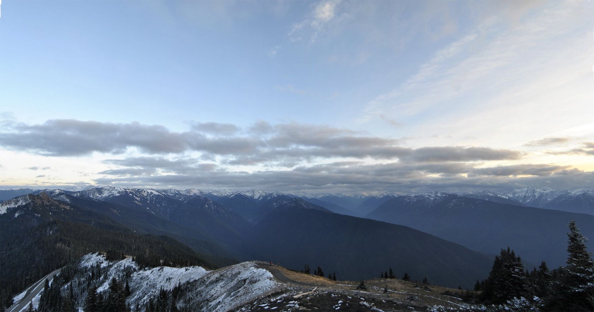 Snow-capped mountain range under a cloudy sky. Light illuminates the horizon.