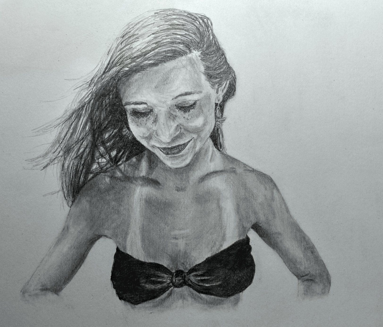 Woman in a black bikini top, looking down with a slight smile. Wind blows through her hair.