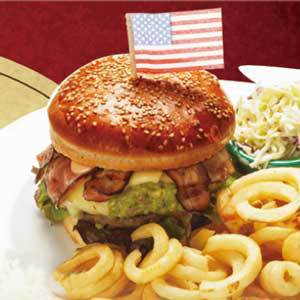 アメリカ国旗が突き出ている皿の上にハンバーガーとフライドポテトが載っている