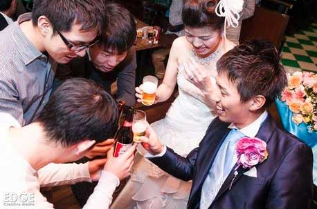 A group of people are toasting a bride and groom at a wedding reception held at a sports bar in Nagoya, Japan.