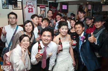 A group of people posing for a picture with a bride and groom holding beer bottles.