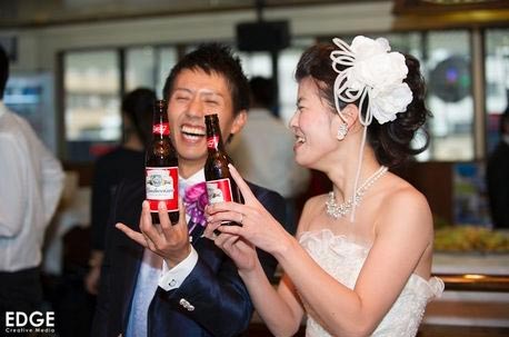 A bride and groom are toasting with two bottles of beer at their wedding after party at Shooters in Nagoya, Japan.