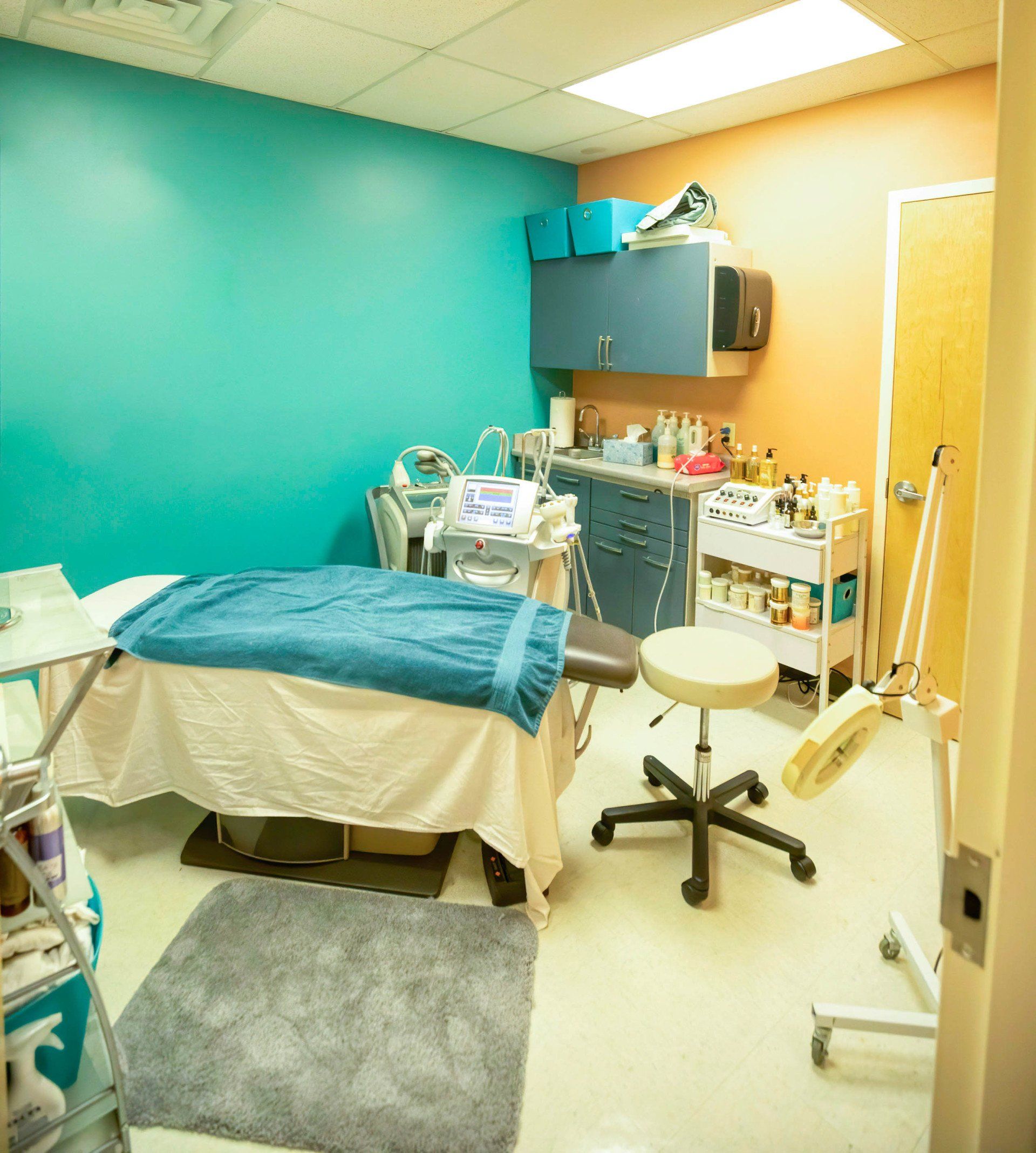 Spa treatment room with teal and orange walls, massage table, and rolling stool.