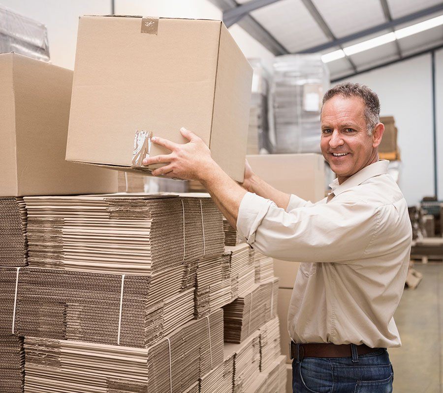 A man is holding a cardboard box in a warehouse.