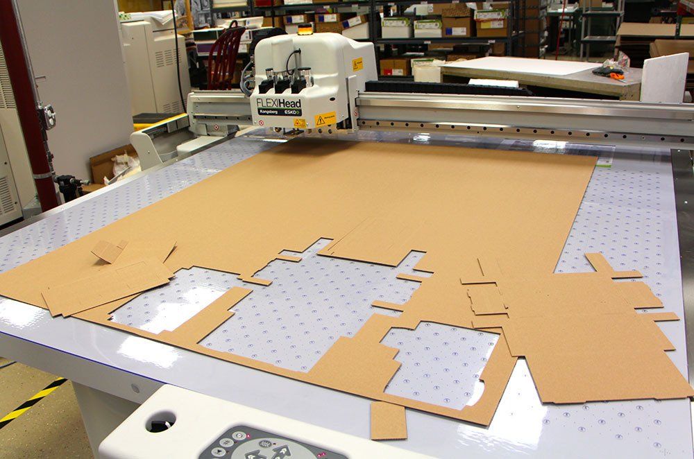 A machine is cutting a piece of cardboard on a table